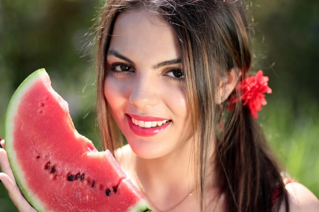 Smiling young woman holding a slice of watermelon, enjoying a sunny day outdoors. 